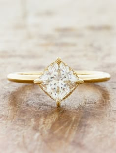 a yellow gold engagement ring with a princess cut diamond in the center on a wooden surface