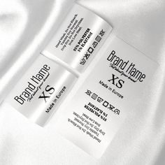 two white business cards laying on top of a white satin material background with the name brand name xs