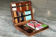 an open wooden box with pens, books and other items in it on the floor