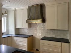 a kitchen with white cabinets and black counter tops, an oven hood over the stove