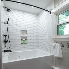 a white tiled bathroom with black fixtures and shower head in the corner, along with two windows