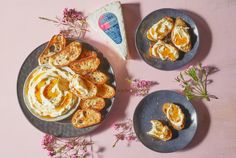 two plates filled with food on top of a pink table next to flowers and cheese