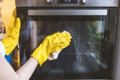 a woman in yellow gloves cleaning an oven with a rag on her mittens