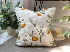 a white pillow sitting on top of a carpet next to a potted plant