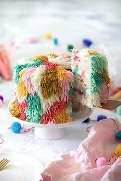 a colorful cake on a white plate with a knife and fork in the foreground