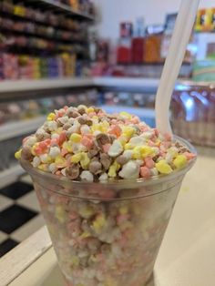 a plastic cup filled with candy corn and marshmallows on top of a checkered counter