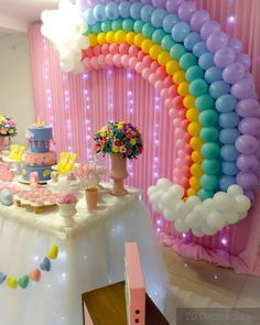 a table topped with cake and balloons next to a rainbow shaped balloon arch on the wall