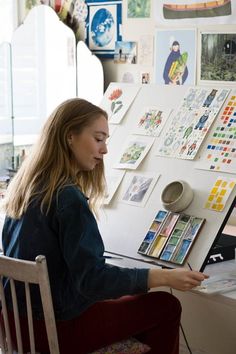 a woman sitting in front of a white refrigerator covered in magnets and stickers