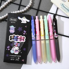 four different colored pens sitting next to each other on top of a white table with pearls