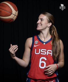 a female basketball player holding a ball in one hand and looking up at the sky