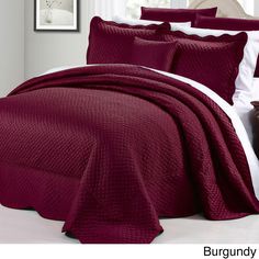 a bed covered in a maroon bedspread and pillows