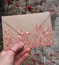 a hand holding an envelope with red flowers on it