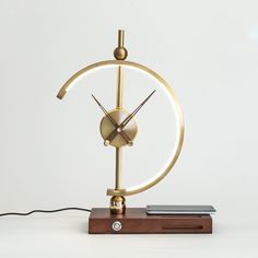 a golden clock on a wooden stand with a white wall in the background and a cell phone sitting next to it