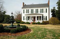 a large white house sitting on top of a lush green field next to a fountain