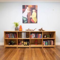 a book shelf filled with lots of books on top of a hard wood floor next to a painting