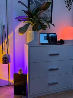 a white dresser with a laptop on top of it next to a potted plant