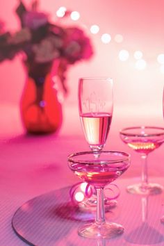 three wine glasses sitting on top of a glass plate with pink lights in the background