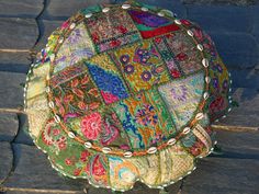 a colorful patchwork round pillow sitting on top of a stone floor next to a brick walkway