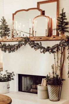 a fireplace decorated for christmas with candles and evergreen garland on the mantel above it