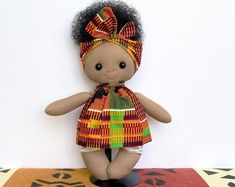 a small doll with an afro hair wearing a colorful dress and headband sitting on a rug