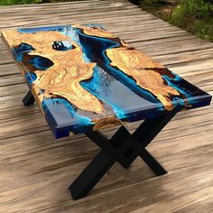 a wooden table with blue and gold paint on it sitting on a wood deck outside