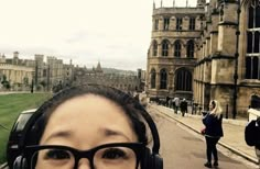 a woman with headphones on standing in front of an old building and looking at the camera