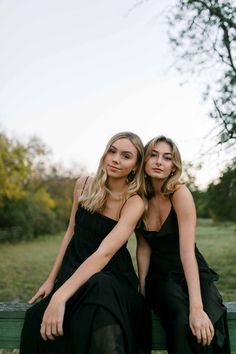 two beautiful young women sitting next to each other on a bench in the park together