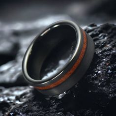 a wedding ring with an orange stripe on it sitting on top of a rocky surface