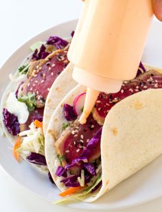 a person is pouring dressing on two tacos with lettuce and carrots