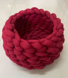 a red rope basket sitting on top of a white tile floor next to a wall