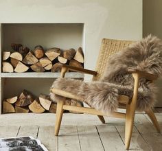 a chair with fur on it in front of firewood logs and a bookcase