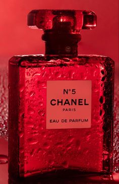 a red chanel bottle sitting on top of a table next to a pink wall