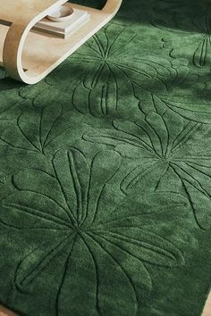 a green rug is on the floor with a wooden table and chair in the background