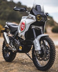 a white and black motorcycle parked on top of a dirt road