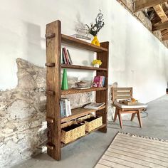 a wooden book shelf sitting next to a chair and table in a room with stone walls