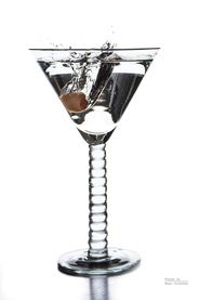 a martini glass filled with water and an olive slice on the rim, in front of a white background