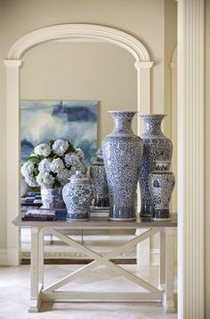 a table with vases and flowers on it in front of a mirror, framed by columns