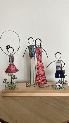 three paper cut people standing on top of a wooden table