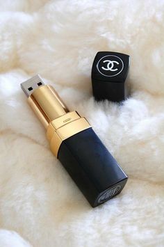 chanel lipstick on white fur with black and gold packaging next to it in the foreground