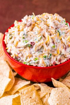 a red bowl filled with chicken salad surrounded by tortilla chips on the side