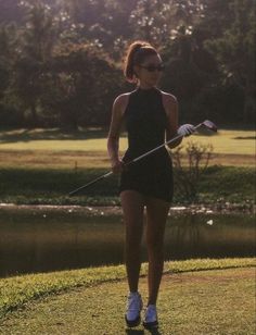 a woman holding a golf club on top of a green field