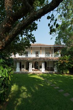 a large white house sitting on top of a lush green field next to a tree