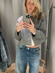 a woman taking a selfie in front of a mirror while wearing jeans and a jacket