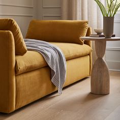 a yellow couch with a blanket on it next to a table and potted plant