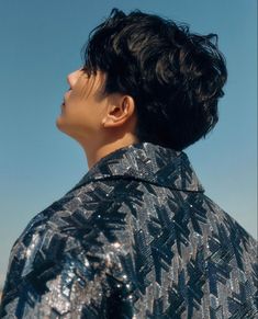 a man with black hair standing in front of a blue sky and looking off into the distance