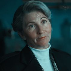 an older woman with grey hair wearing a white turtle neck sweater and black blazer