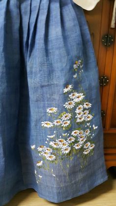 a blue skirt with white daisies on the front and bottom, sitting next to a wooden cabinet