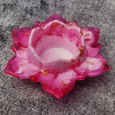 a pink flower shaped bowl sitting on top of a cement floor next to a wall