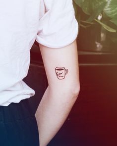 a person with a coffee cup tattoo on their left arm and the other hand is holding a potted plant