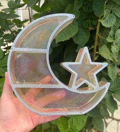 a person holding up a clear glass object with a star and moon cut out of it